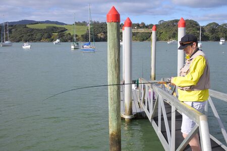 Mature adult man (age 30-40) fishing with a fishing rod from a boat jetty. Real people. Copy space