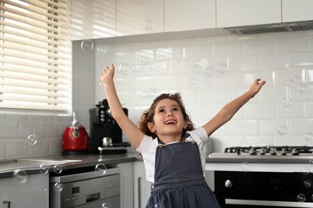 Happy girl (age 06) playing with soap bubbles at home kitchen. Real people. Copy spaceの写真素材