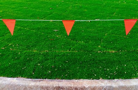 A warning red triangular shape flags hanged on a wire to protect new installed fresh natural green grass rugs.の写真素材