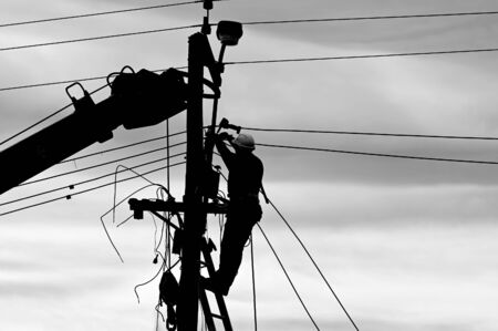 Silhouette of unrecognizable  electricity worker fixing power line on stormy winter day.の写真素材