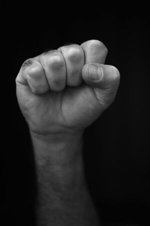 Male raised fist isolated on black background. The clenched fist, is a symbol of solidarity and support.It is also used as a salute to express unity, strength, defiance, or resistance.の写真素材