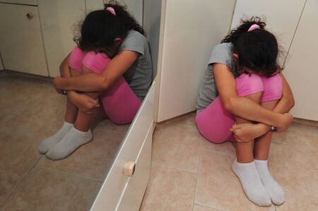 Young girl sitting in the corner of home kitchen foor.の写真素材