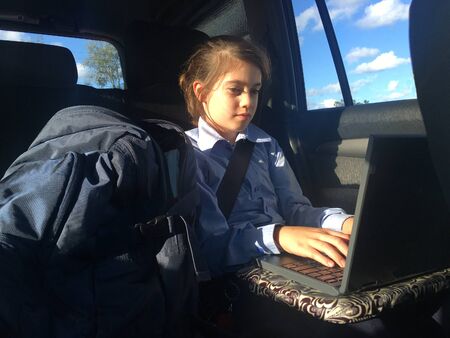 Schoolgirl (age 10) using laptop in a car after school.