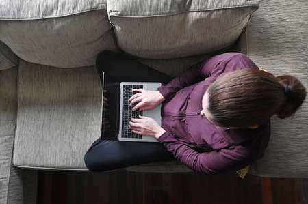 Aerial view of a young woman using a laptop on a couch working from home. Real people. Copy spaceの写真素材