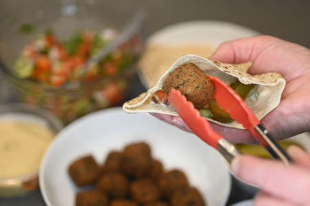 Person filling pitta bread with falafel ball and Middle Eastern salads.