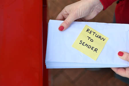 Above view of unrecognizable woman sending return to sander letters in envelope in red mail boxの写真素材
