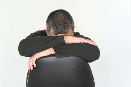 Sad adult man sitting on office chair covering his face.の写真素材