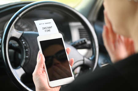 Adult woman (age 30-40) using mobile phone while driving a car is receiving an instant fine from the...