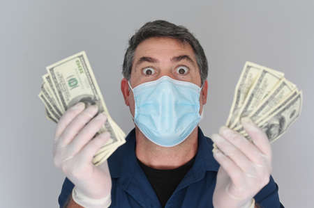 Happy adult man wearing a face mask holding a large sum of Federal Reserve Bank Notes payments looking at camera.の写真素材
