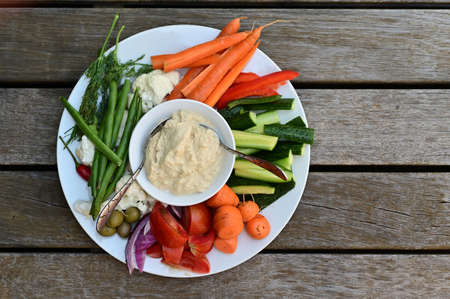 Flat lay view of Hummus dip and fresh vegetables salad served on in a plate on outdoor wooden table.