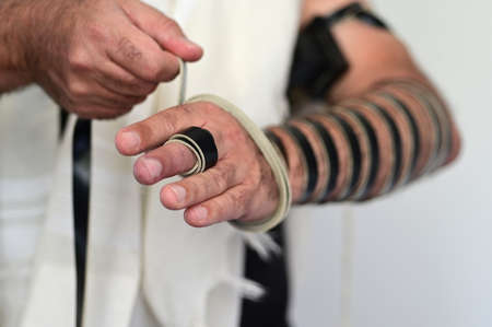 Close up of a Jewish man wrapping himself with with Tefillin (phylacteries) on morning prayers.