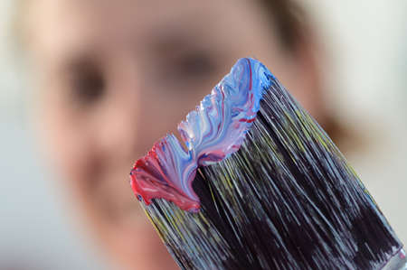 Happy woman face looking at colorful paint on a paint brush isolated abstract background and textureの写真素材