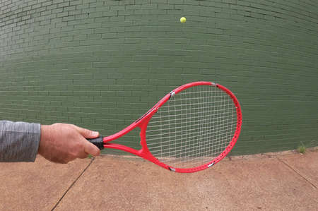 POV (point of view) of a person playing wall tennis hitting a tennis ball with tennis racket.の写真素材