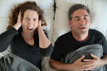 Upset mature adult man (male age 40-50) suffering from his partner an adult woman (female age 30-40)  that snoring during sleep in bed. Couple lifestyle and people health care concept.の写真素材