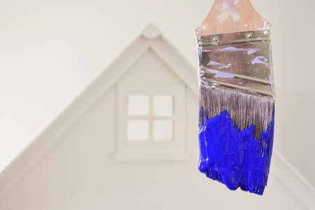 Paint brush with blue paint color against a white house. Renovation, home decoration and painting house concept. No people. Copy spaceの写真素材