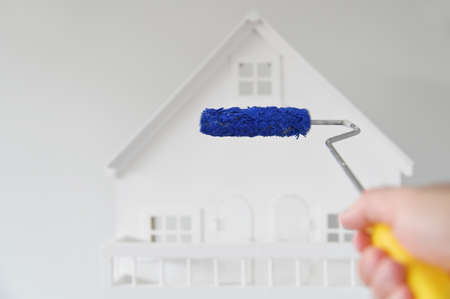 POV (point of view) of a person holding a paint roller brush with blue color against a white house. Renovation, home decoration and painting house concept. No people. Copy spaceの写真素材