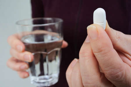 Close up of female hands holding a medication pill with glass of water.