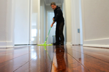 Adult man mopping a wooden floor at home corridor. Focus on foregroundの写真素材