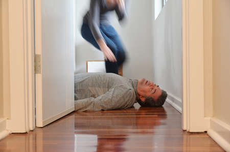 Adult woman rushing to help a mature adult man (male age 40-50) lying on bedroom floor unconscious.の写真素材