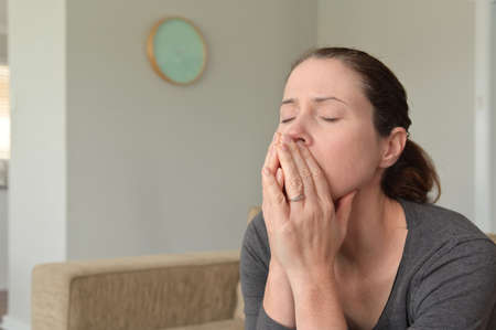 Upset adult woman (female age 30-40) sitting on a couch alone with closed eyes and puzzled face...