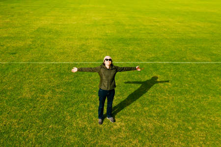 Aerial view of happy active adult woman looking up with open arms on a green grass.の写真素材