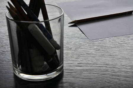 Group of pencils in a glass jar in front of a pencil on white paperの写真素材