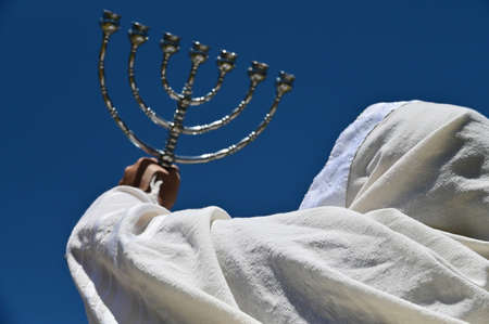 Rear view of orthodox Jewish man holding a Menorah against clear blue sky.