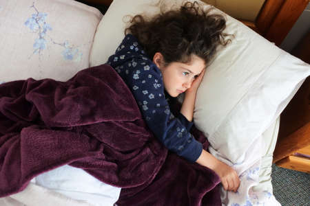 Aerial view of sad young girl (female age 07-08) lying in bed.
