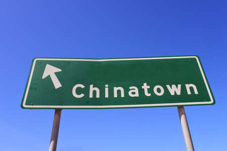 Arrow pointing the direction  to Chinatown on a green and white traffic sign isolated on clear blue sky.の写真素材