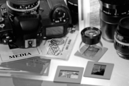 Photojournalist table with media and press pass credentials cards beside a professional camera, photography lenses and a loupe on slides in the backgroundの写真素材