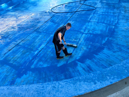 KATIKATI, NZL -  MAR 05 2025:Maintenance person cleaning a swimming pool with broom.Swimming pool contaminants are introduced from environmental sources and swimmers include windblown dirt and debris.の写真素材