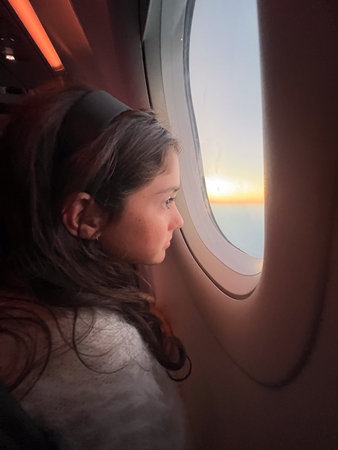 Cute young air passenger girl (female age 11-12) sit inside airplane flying away to an exotic travel holiday vacation, smiling happily while looking backwards at camera. Real people. Copy spaceの写真素材