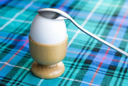 White egg arranged with silver teaspoon on a colorful kitchen table