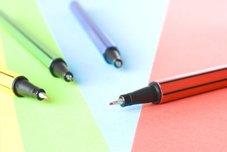 Colorful pens arranged on colorful paper background. Selective focus on red pen only.