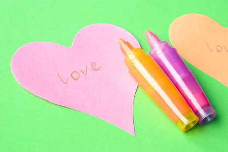 Word LOVE written on a pink heart arranged with colorful felt tip pens and green background. Love concept.の写真素材