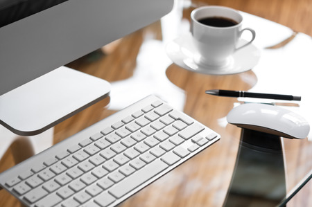 Glass desk with modern computer and cup of coffeeの写真素材