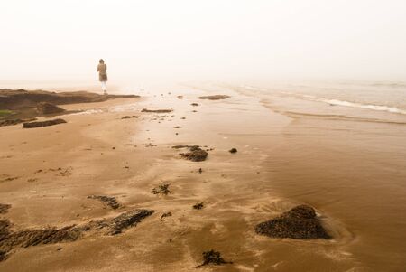 Woman walking away into fog at the sea shoreの写真素材