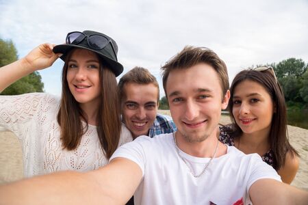 A group of four young adult friends taking selfie on sandy beach