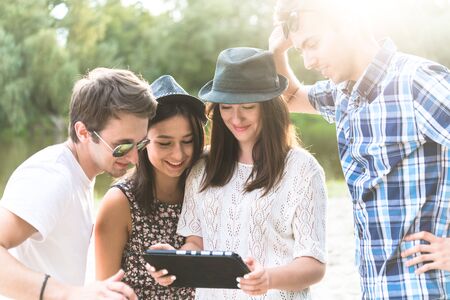 Young adult friends taking selfies with tablet and having fun outdoorsの写真素材