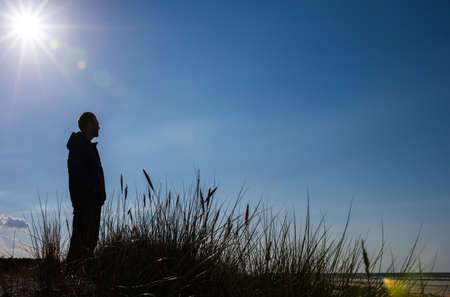 Silhouette of man standing on sand dune looking at sea and relaxingの写真素材