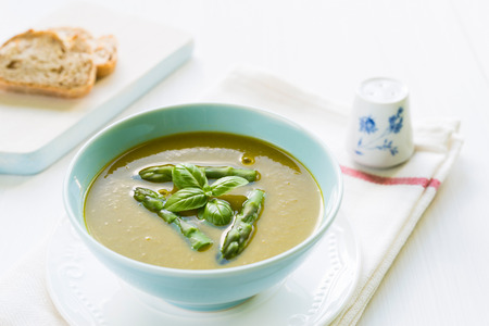 Close up of asparagus soup in a bowl with basil, bread and salt shakerの写真素材
