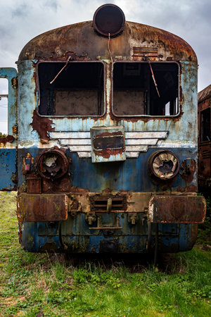 Old rusty electric multiple unit train decommissioned and abandoned on railway siding on green...