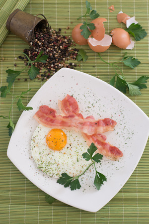 Close-up of delicious fried egg breakfast with bacon. With warm green background.の写真素材