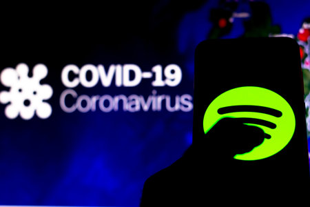 April 8, 2020, Brazil. In this photo illustration the Spotify logo seen displayed on a smartphone with a computer model of the COVID-19 coronavirus in the background.のeditorial素材