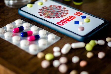 In this photo illustration pharmaceutical pills are seen displayed on a table with a COVID-19...