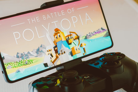 November 11, 2023, Brazil. In this photo illustration, the Battle of Polytopia logo is displayed on a smartphone screen, next to a gamepad. Billionaire Elon Musk recently said that he calms his mind by playing this video gameのeditorial素材