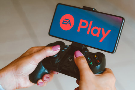 December 4, 2023, Brazil. In this photo illustration, the EA Play logo is displayed on a smartphone screen as a person plays on a gaming gamepadのeditorial素材