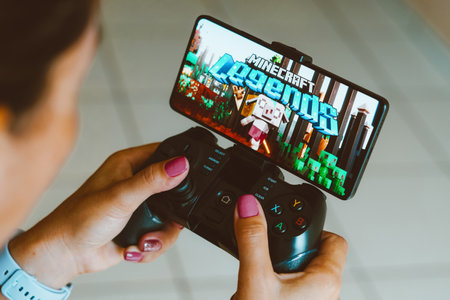 December 4, 2023, Brazil. In this photo illustration, the Minecraft Legends logo is displayed on a smartphone screen as a person plays on a gaming gamepadのeditorial素材
