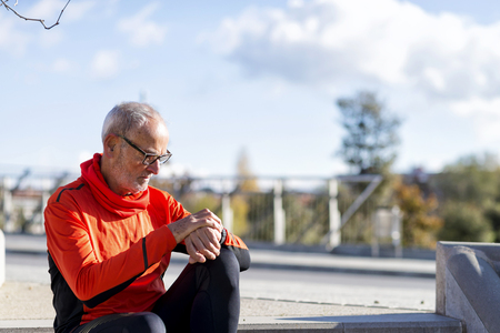 One senior runner man sitting and looking at smartwatch during training. He is satisfied with results.の写真素材