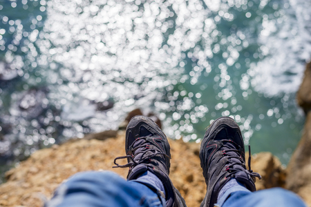 Young brave man sitting on a high cliff above calm seaの写真素材